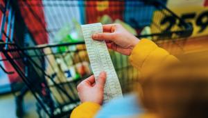 Color photo of customer looking at receipt with grocery cart in the background
